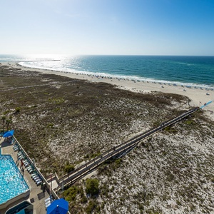 Crystal clear water sparkles by the pool as you gaze across the beach and stretch of dunes from your balcony