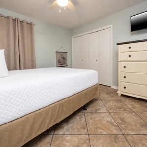 Guest bedroom featuring a comfortable queen bed, soft beige curtains, and a flat-screen TV for relaxing evenings