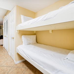 This cozy bunk area features two neatly made beds and offers a glimpse of the inviting beach view beyond