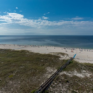 Expansive view of the beach with colorful umbrellas, soft white sand, and tranquil gulf waters under a bright blue sky