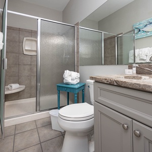Guest bathroom featuring a walk-in shower, decorative turquoise accents, and neatly arranged towels on a stylish stool