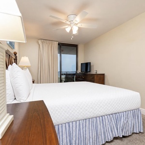 Bright and airy master suite featuring a king bed, a ceiling fan, and the beachfront balcony with stunning views
