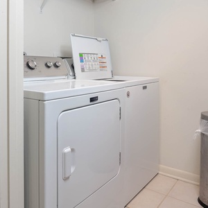 Laundry area featuring a washer and dryer, with a trash can nearby and a shelf for storage above
