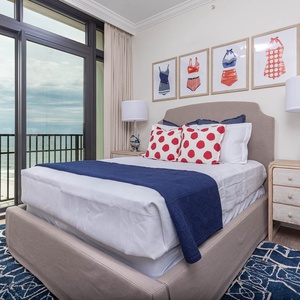 This bedroom features a cozy queen bed with playful polka dot pillows and stunning beachfront views through large glass doors