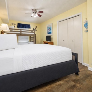 The yellow walls complement the cozy guest bedroom featuring a queen bed, a twin/full bunk bed, and nautical-themed decor