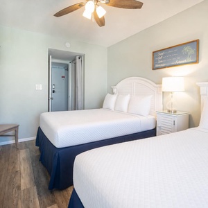 This guest bedroom features two comfortable beds, a mounted TV, and a soothing color palette for a relaxing stay