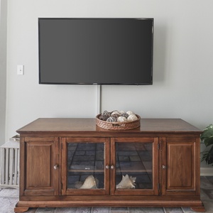 Wooden media console with decorative bowl, flat-screen TV, and a potted plant beside a glass door leading to the balcony