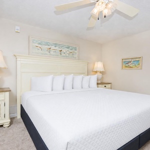 The bedroom featuring a large king bed with plush white linens, complemented by soft lighting and coastal artwork