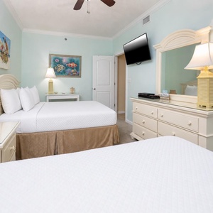 Bright guest bedroom featuring two double beds, a wall-mounted TV, and coastal artwork, creating a cheerful atmosphere