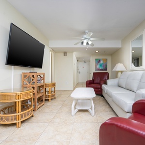 The living area features a large TV, stylish white leather sofa, and vibrant red accent chairs, perfect for relaxation