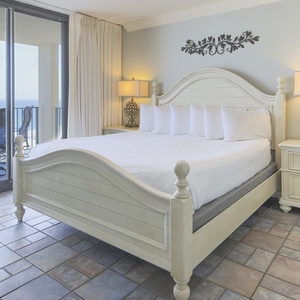 Master bedroom features a king bed, elegant decor, and sliding doors opening to a balcony with a beautiful beach view