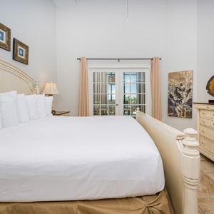 The master bedroom features a plush king bed, elegant decor, and a TV, with beautiful views through French doors