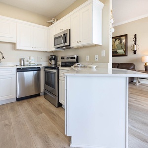 White cabinetry complements the modern kitchen, featuring a breakfast bar and stainless appliances