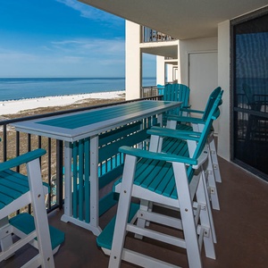 Balcony features a tall table with turquoise seating, offering a serene view of the beach and calm gulf waters