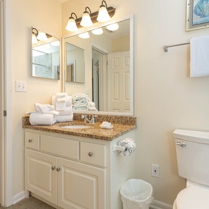 Bright bathroom features a granite countertop, ample towels, and a view into a cozy living area with a blue sofa