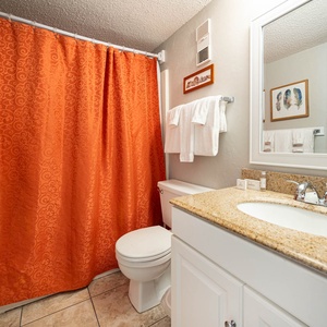 The bathroom features a orange shower curtain, a spacious vanity with a granite countertop, and fresh towels