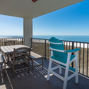 Balcony with a dining table and teal chairs offers a serene view of the gulf and the beach below, perfect for relaxation