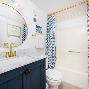 The guest bathroom features a stylish navy cabinet, elegant gold fixtures, and a large round mirror, creating a chic retreat