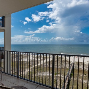 Balcony seating offers a serene view of the beach and gulf, framed by a bright blue sky and gentle waves
