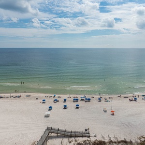 Panoramic view showcases a pristine beach with colorful umbrellas and sunbathers against a backdrop of calm waters