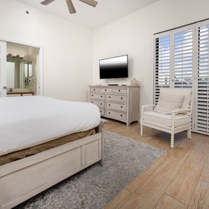 Bright and airy master featuring a king bed, a TV, and a cozy chair beside balcony windows