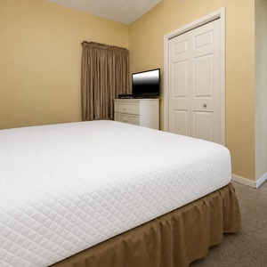Cozy bedroom features a plush king bed, a TV on a dresser, and soft beige walls with elegant drapery