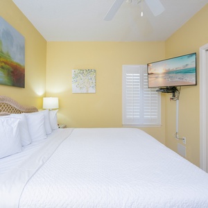 A cozy bedroom features a plush king bed, a wall-mounted TV, and soft yellow walls, creating a warm and inviting atmosphere