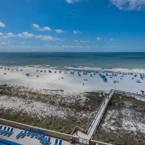 The view showcases a pristine beach with white sand, colorful umbrellas, and a pool area lined with lounge chairs