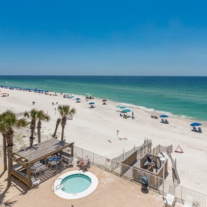 This stunning view showcases a beachfront scene with blue umbrellas, palm trees, and a relaxing hot tub area