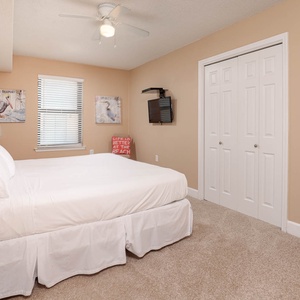 The guest bedroom features a king bed, light-colored walls, decorative artwork, and a wall-mounted TV for entertainment