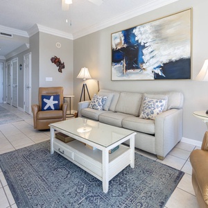 Bright living area featuring a light gray sofa with queen sleeper, a glass-top coffee table, and a cozy accent chair