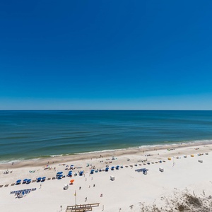 Vibrant beach scene features white sand, colorful umbrellas, and sunbathers enjoying the sunny shoreline
