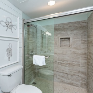 The master bath features a walk-in shower with glass doors, elegant stone tiles, and nautical-themed artwork on the walls