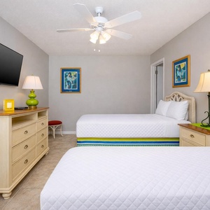 This guest bedroom features two beds with colorful bedding, a mounted TV, and cheerful decor, perfect for a relaxing stay