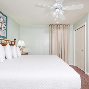 Brightly decorated bedroom featuring a king bed with fluffy pillows, a lamp, and soft curtains for a relaxing atmosphere
