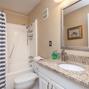 The master bathroom features a stylish granite countertop, a sleek mirror, and a striped shower curtain for a fresh feel