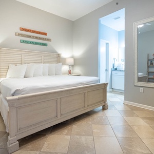 Coastal master bedroom features a king bed, decorative wall signs, and a view of the adjoining bathroom area
