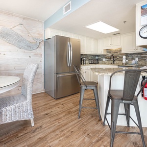 Bright and airy kitchen area features a granite countertop, modern appliances, and a cozy dining space with woven chairs