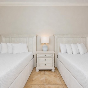 Bright and airy guest bedroom featuring two cozy queen beds, a stylish nightstand, and soft white linens for a restful stay