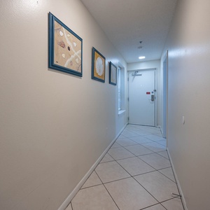 A welcoming hallway features framed coastal art, tile flooring, and natural light streaming through a nearby window