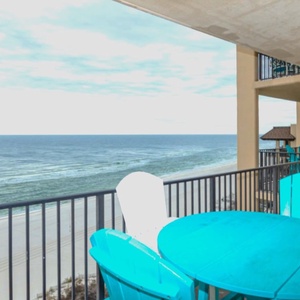 A vibrant turquoise table and chairs offer a perfect spot to enjoy the breathtaking beachfront view from the balcony