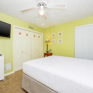 Relaxing guest bedroom featuring a queen bed, wall-mounted TV, and charming coastal decor in soft green hues