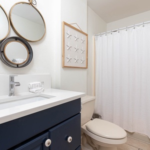 The bathroom features a sleek navy vanity, stylish mirrors, and a serene starfish decor, creating a refreshing atmosphere
