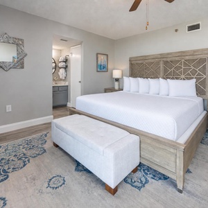 Master bedroom featuring a king bed with plush bedding, a stylish bench, and a modern en-suite bathroom visible
