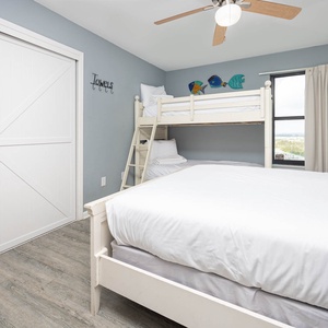 This guest bedroom features a queen bed, a charming twin bunk bed, and colorful fish decor, perfect for a family getaway