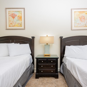 This bedroom features two comfortable queen beds, decorative artwork, and a stylish lamp for a relaxing stay