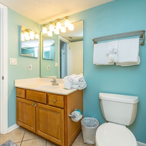 Light blue walls complement the wooden vanity in this bathroom, featuring ample counter space and neatly arranged towels