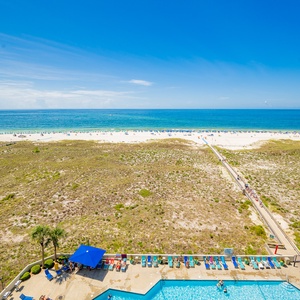 Balcony view of the beach and gulf from the balcony, featuring a pool area with lounge chairs and vibrant umbrellas