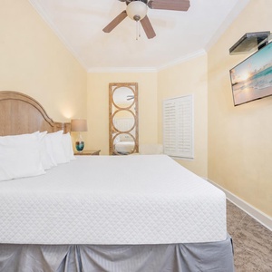 Guest bedroom featuring a plush king bed, soft yellow walls, and a wall-mounted TV for entertainment