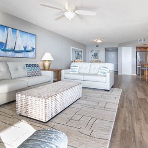 Living area features a white leather sofa with decorative pillows, a textured coffee table, and a view into the kitchen
